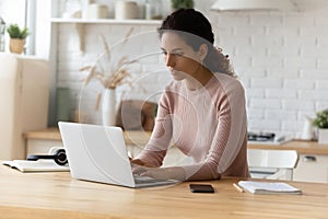 Millennial latina woman work online using laptop at home kitchen