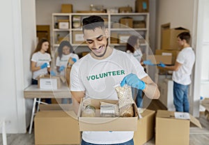 Millennial male volunteer working at charity center, holding food donation box, proud of working at charity center