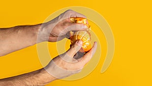 Millennial man peeling juicy orange on color background, closeup with blank space. Panorama