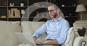 Millennial man sit on sofa working online using laptop