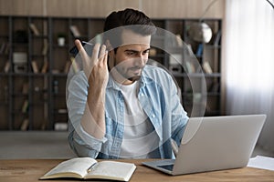 Millennial man student using smartphone loudspeaker read ebook from laptop
