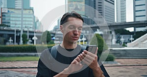 Millennial man tourist with backpack using mobile phone while explore city street. Male tourist traveling at big city