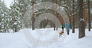 A millennial man trains a dog in a snowy winter forest.