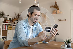 Millennial man using card and phone to provide payment online photo