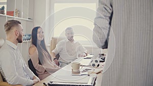 Millennial office workers sit by the table and smile, listening to unrecognisable female team leader giving a speech 4K.