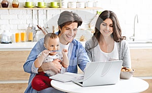 Millennial parents with baby son working on laptop at kitchen