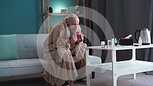 Millennial sick man sitting on sofa drinking tea suffering from influenza
