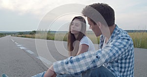 Millennial teens sitting on skateboard at camera and having joy during a talk