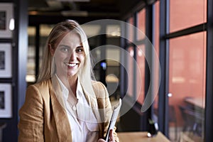 Millennial white blonde businesswoman smiling to camera by the window in an office, close up photo