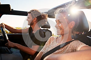 Millennial white couple on a road trip driving in an open top car, backlit, close up