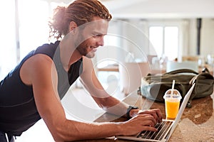 Millennial white man checking fitness app on laptop at home after a workout, side view