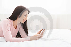 Millennial woman browsing on cellphone, lying on bed