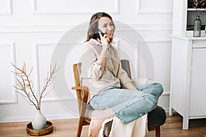 Millennial Woman Smiling, Speaking on Phone, Sitting on Chair, Looking Out Window at Free Space. Smiling millennial