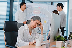 Millennial young Chinese businesswoman working stress out with project research problem on computer desktop in meeting room at