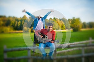Millennials, cheerful young couple playing guitar and singing in nature