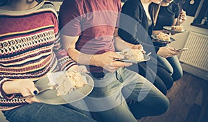 Millennials friends sit on kitchen chairs and eat homemade cake. At the same time, they send sms and share data on social media.