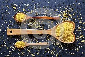 Millet groats in wooden spoons on black table