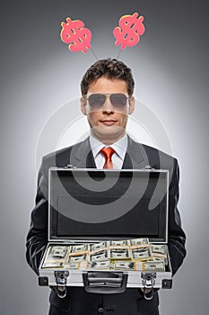 Millionaire. Confident man in formal wear holding a suitcase full of money while standing isolated on gray