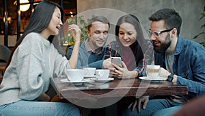 Milti-ethnic group of friends using smartphone talking and laughing in cozy cafe