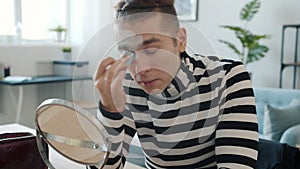 Mime atrist putting on face paint looking at mirror using make-up at home