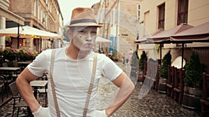 Mime in hat looks bold, cocky, walks proudly with hands akimbo.