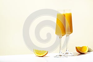 Mimosa alcohol cocktail drink with orange juice and cold dry champagne or sparkling wine in glasses. Beige background, hard light