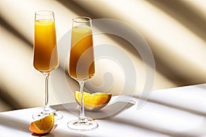 Mimosa alcohol cocktail drink with orange juice and cold dry champagne or sparkling wine in glasses. Beige background, hard light