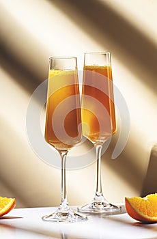 Mimosa alcohol cocktail drink with orange juice and cold dry champagne or sparkling wine in glasses. Beige background, hard light