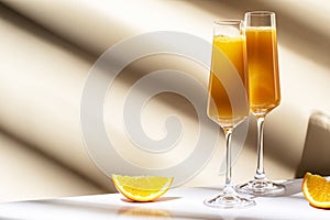 Mimosa alcohol cocktail drink with orange juice and cold dry champagne or sparkling wine in glasses. Beige background, hard light