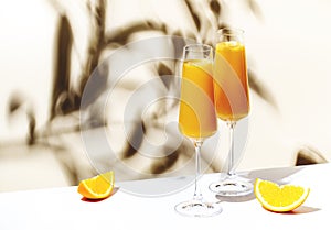 Mimosa summer cocktail drink with orange juice and cold dry champagne or sparkling wine in glasses. Beige background, hard light,