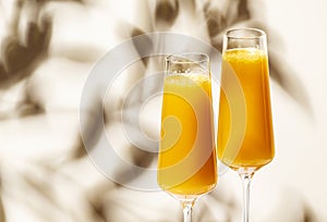 Mimosa summer cocktail drink with orange juice and cold dry champagne or sparkling wine in glasses. Beige background, hard light,