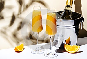 Mimosa summer cocktail drink with orange juice and cold dry champagne or sparkling wine in glasses. Beige background, hard light,