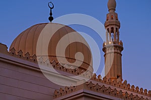 Minaret and dome of Muslim Islamic mosque on sunset background. Minaret tower and roof cupola with traditional crescent