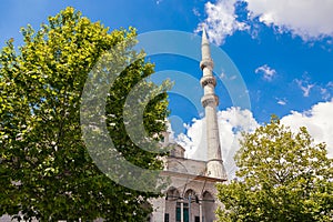 Minaret of Eminonu New Mosque or Yeni Cami with trees and partly cloudy sky