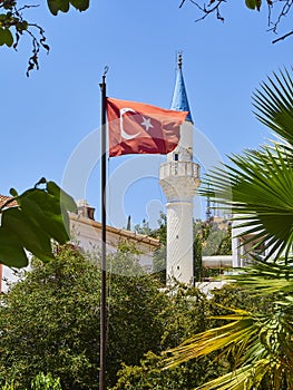 Minaret of Kelerlik Mahallesi Cami mosque with the flag of Turkey waving in foreground.