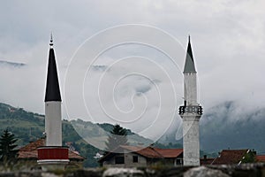 Minarets in a small town on the background of lush green hillside shrouded in fog