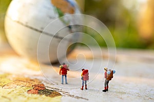 Minature people: traveling with a backpack standing on vintage world map and globe,  Travel and vacation concept. photo