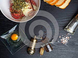 minced meat, bread slices, spices, pepper, egg on wood background, empty space. Prepared ingredients for cooking differently