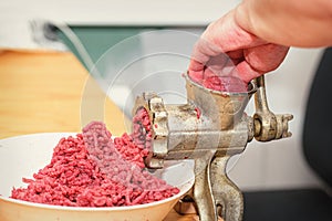 Minced meat. Woman`s hands twist manual meat grinder through which minced meat comes out.