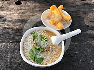 Minced pork congee with deep fried garlic and vegetable in white bowl. Serve with deep fried dough stick.