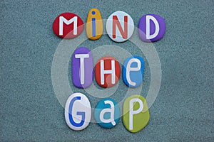 Mind the gap, creative logo composed with multi colored stone letters ovver green sand