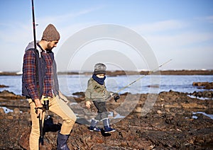 Mind your step. a father and son walking on the rocks while out fishing together by the sea.