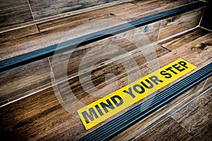 Mind your step sticker sign pasted on wooden stair. Warnings, abstract, or indoor architecture concept