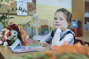 A minded schoolgirl of primary classes sits at a desk and listens to a lesson