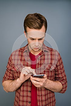Minded serious young man typing message on smartphone