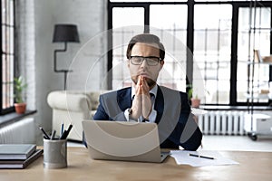 Mindful businessman wearing glasses joining hands in prayer, making wish