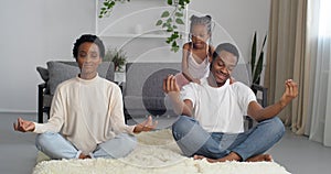 Mindful father dad and mother mom meditating sitting on floor while active energetic child daughter jumping playing