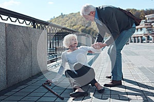 Mindful man helping elderly female stranger to stand up photo