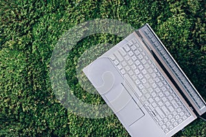 Mindfulness, biophilic design, unplug concept. Computer, laptop keyboard over green grass, moss forest background. Top