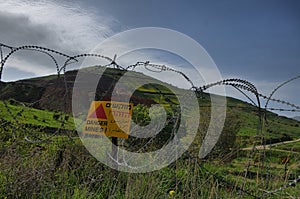 Minefield danger mines yellow warning sign on a barbed wire fence in the Golan Heights, Israel